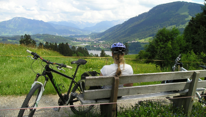 Hansaton: A woman is sitting on a bench and looking at the landscape, her bicycle is next to her.
