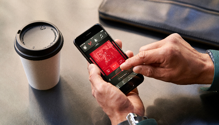 ReSound: Smartphone in hand, the other hand typing in the app, next to it a coffee mug.