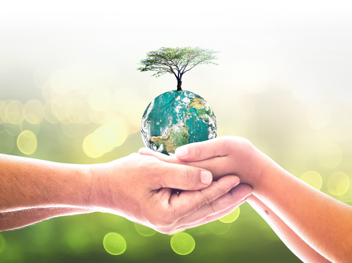 Rechargeable vs Battery Hearing Aids: 6 Key Factors to Help You Decide 7 Two pairs of hands, one adult and one child, gently holding a small Earth globe with a tree growing on top, symbolizing environmental protection and intergenerational responsibility, set against a bright, blurred green background.